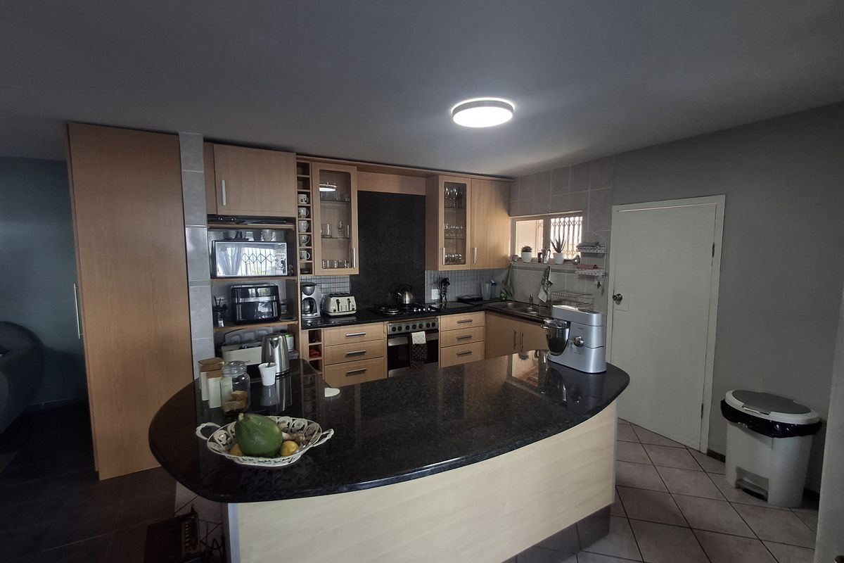 A functional kitchen featuring wood-finish cabinetry, dark granite countertops, a breakfast bar, and integrated cooking appliances with tiled flooring.