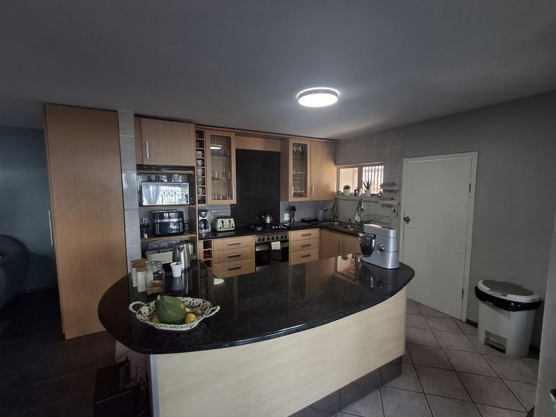 A functional kitchen featuring wood-finish cabinetry, dark granite countertops, a breakfast bar, and integrated cooking appliances with tiled flooring.