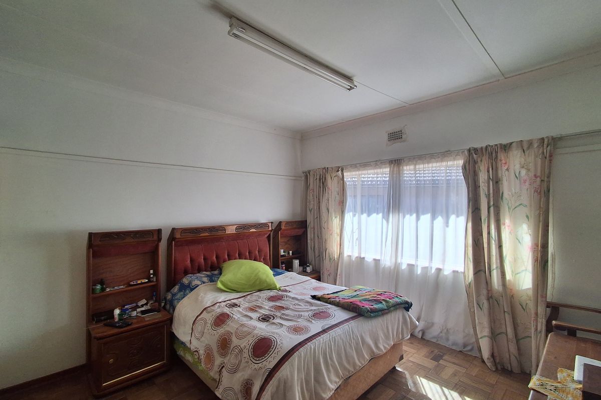 A bedroom featuring parquet flooring, a central fluorescent light fixture, and natural light through a window with curtains.