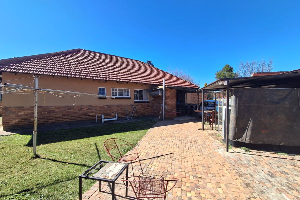 Rear view of the house featuring a brick facade, tiled roof, and a paved patio area with a covered section.