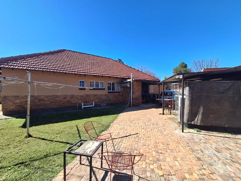 Rear view of the house featuring a brick facade, tiled roof, and a paved patio area with a covered section.
