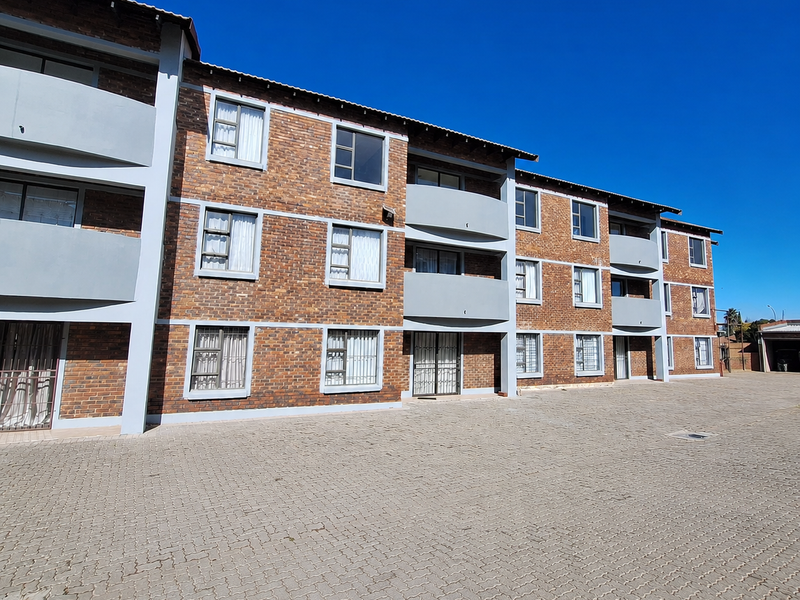 A view of the townhouse complex exterior featuring a face brick facade, paved driveway, and multiple balconies with security features.