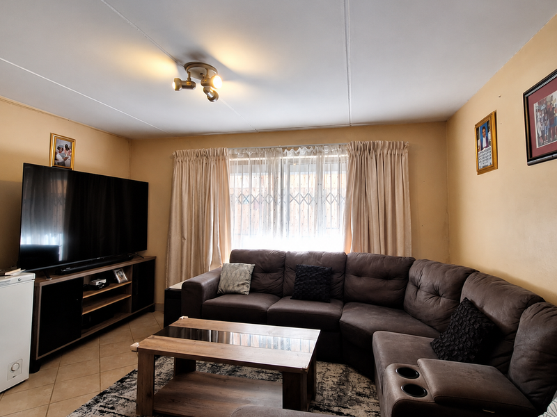 A comfortable living room featuring tiled flooring, a central ceiling light fixture, and a window fitted with a security gate.