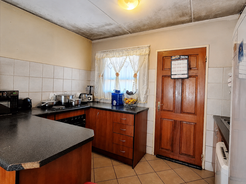 A dated kitchen featuring wooden cabinetry, tiled backsplash, and flooring. The space shows signs of ceiling water damage and requires cosmetic updates.