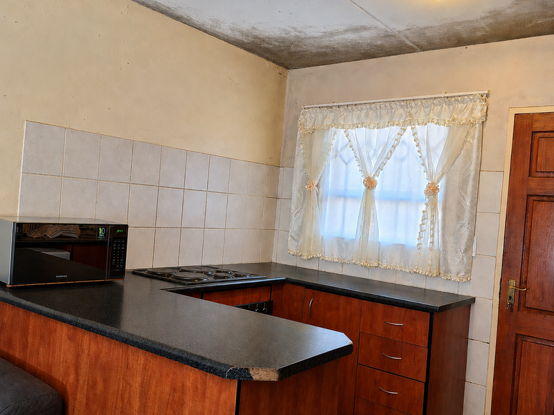 A dated kitchen featuring wood-finish cabinetry, a dark laminate countertop with an integrated hob, and a tiled backsplash, requiring cosmetic updates and ceiling repairs.