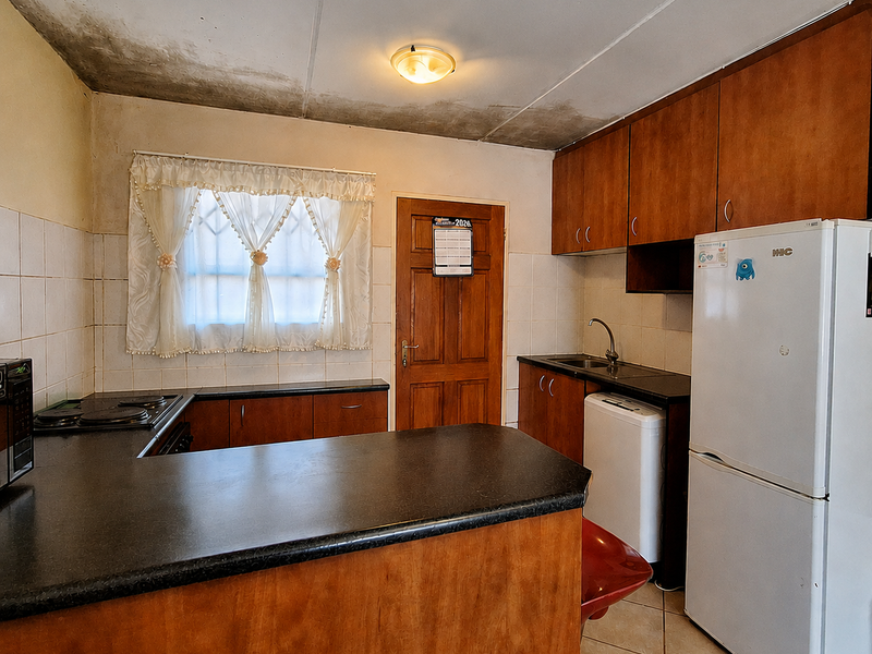 A dated kitchen featuring wood-finish cabinetry, dark countertops, and tiled backsplash, currently showing significant signs of ceiling water damage requiring repair.