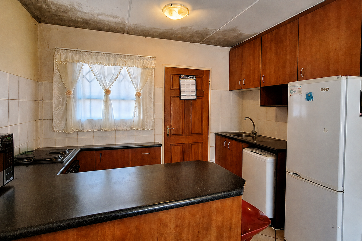 A dated kitchen featuring wood-finish cabinetry, dark countertops, and tiled backsplash, currently showing significant signs of ceiling water damage requiring repair.