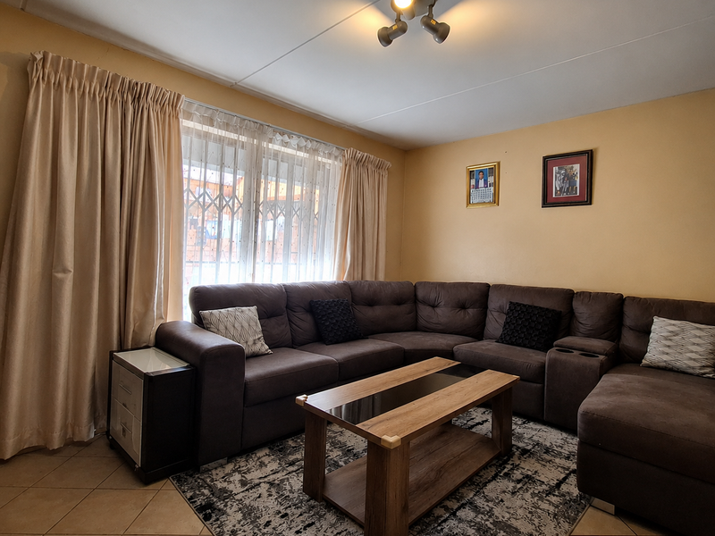 A comfortable living room featuring tiled flooring, a ceiling-mounted spotlight fixture, and a large window fitted with a security gate.