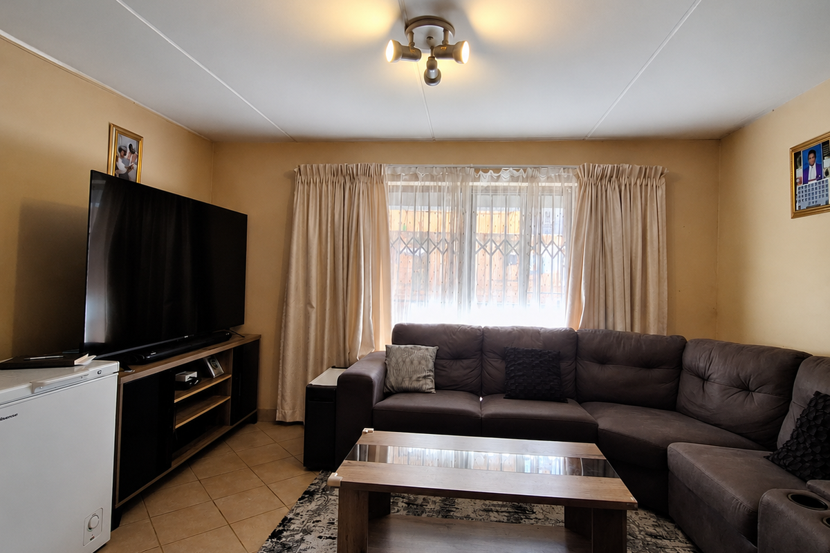 A comfortable living room featuring tiled flooring, a central ceiling light fixture, and a window fitted with a security gate and curtains.
