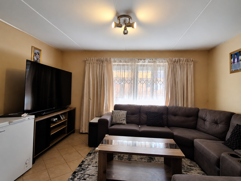 A comfortable living room featuring tiled flooring, a central ceiling light fixture, and a window fitted with a security gate and curtains.