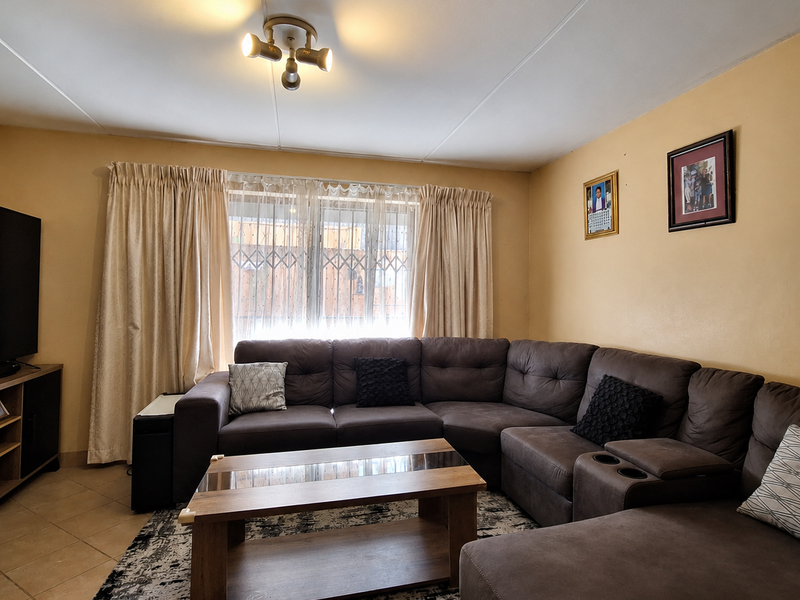 A comfortable living room featuring tiled flooring, a security gate on the window, and a central ceiling light fixture.