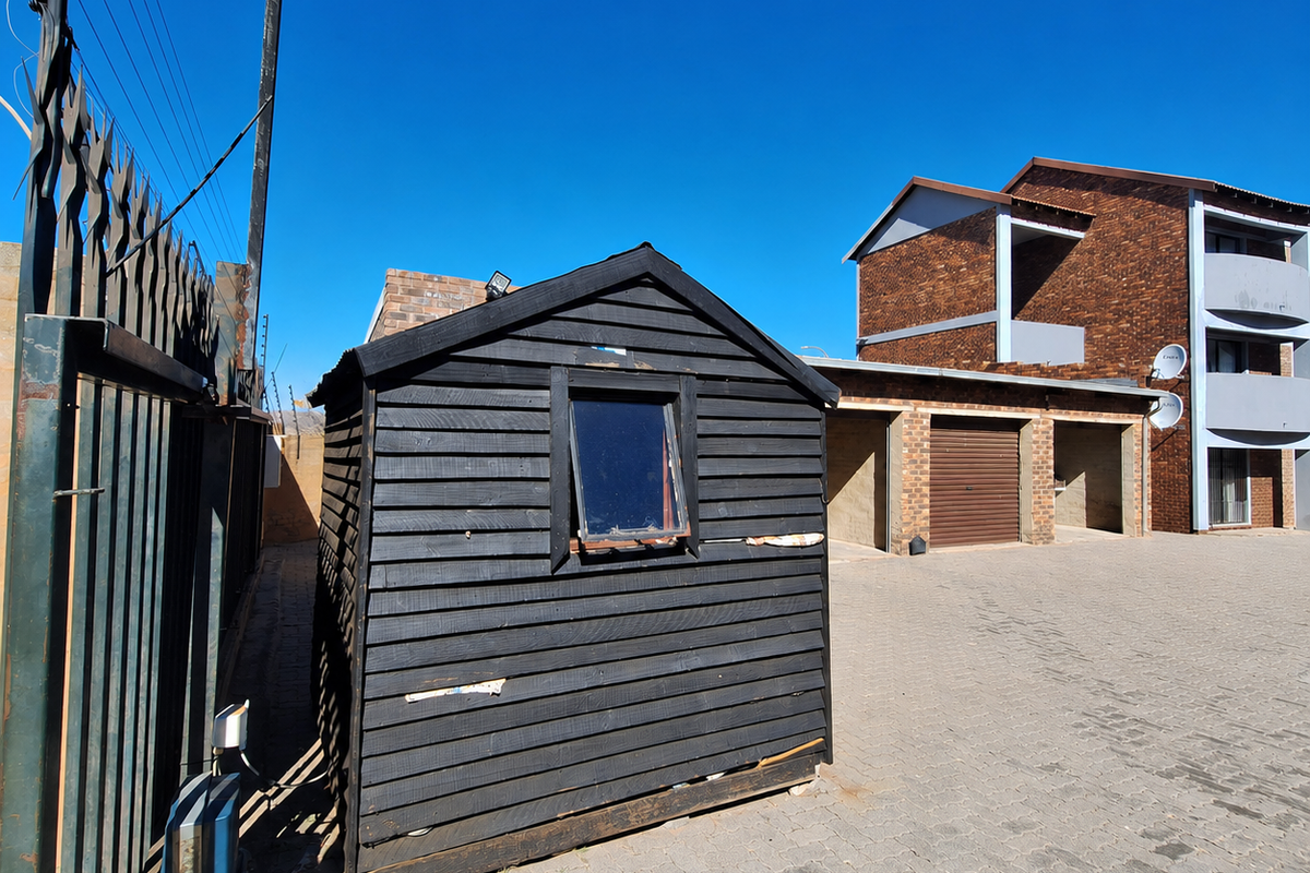 Rear exterior view showing a paved driveway, garage access, and a detached timber storage shed with electric perimeter fencing.