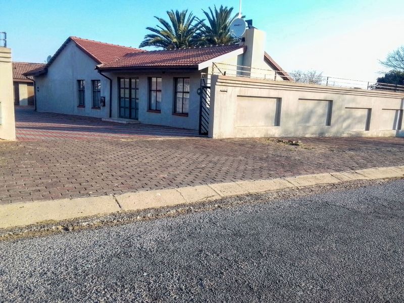 Front exterior view of a single-story house featuring a paved driveway, perimeter wall with security fencing, and a tiled roof.