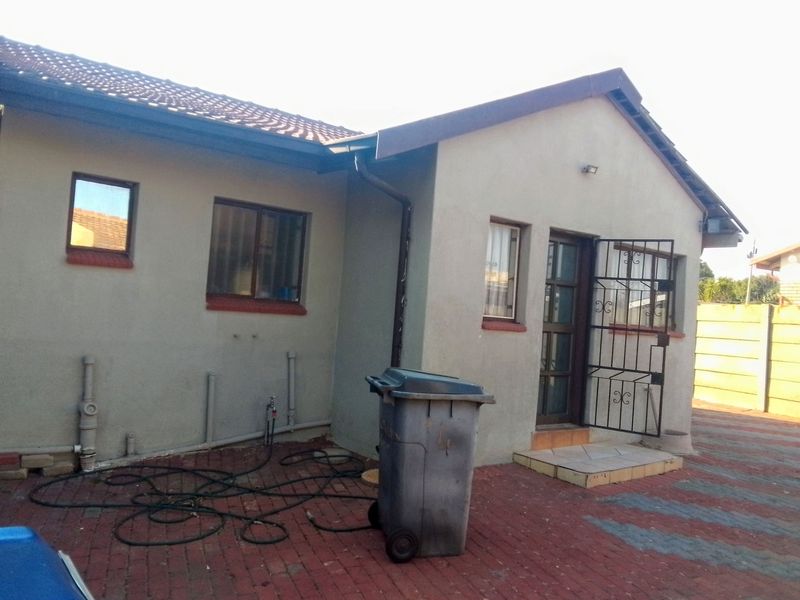 Rear exterior view of the house featuring a paved area, security gate, and tiled roof structure.