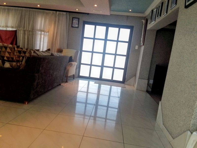 A living room featuring polished tiled flooring, recessed ceiling lighting, and a large grid-pattern glass door providing natural light.