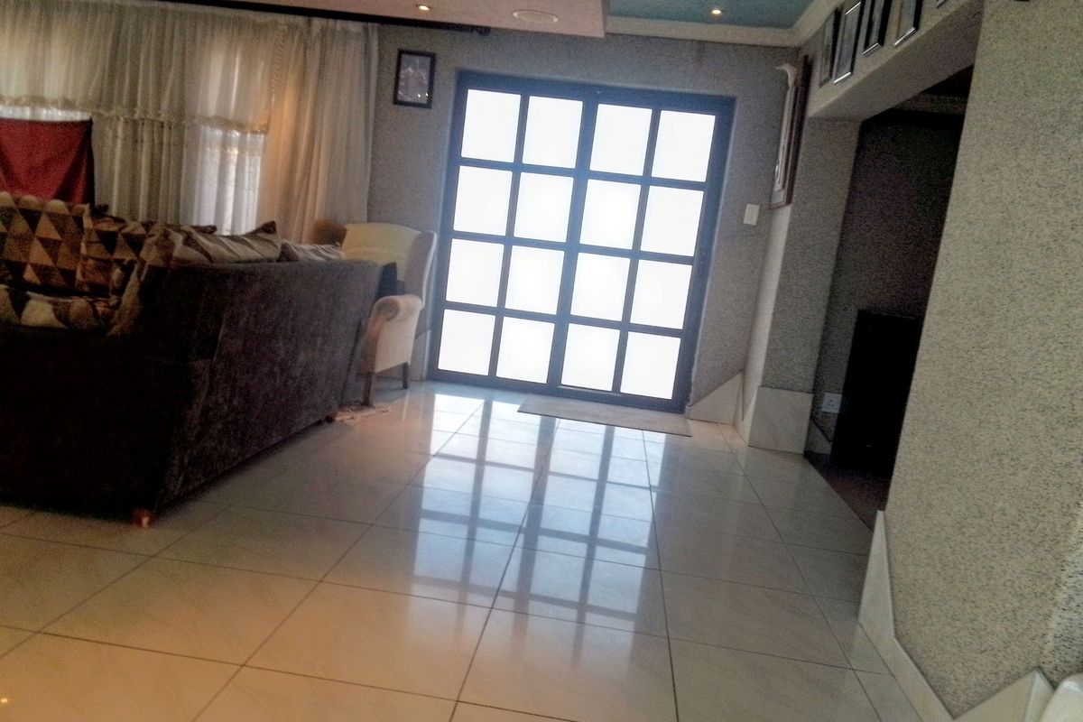 A living room featuring polished tiled flooring, recessed ceiling lighting, and a large grid-pattern glass door providing natural light.
