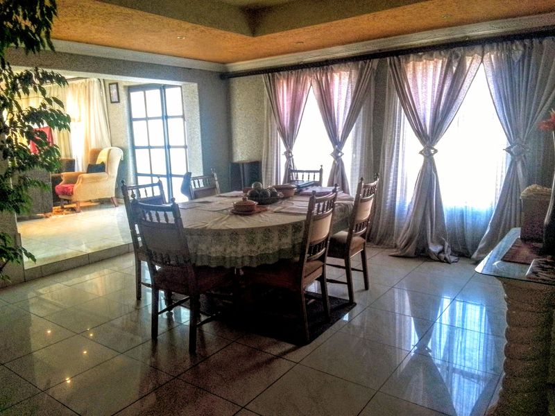A dining room featuring polished tiled flooring and a recessed ceiling, with large windows allowing for natural light.