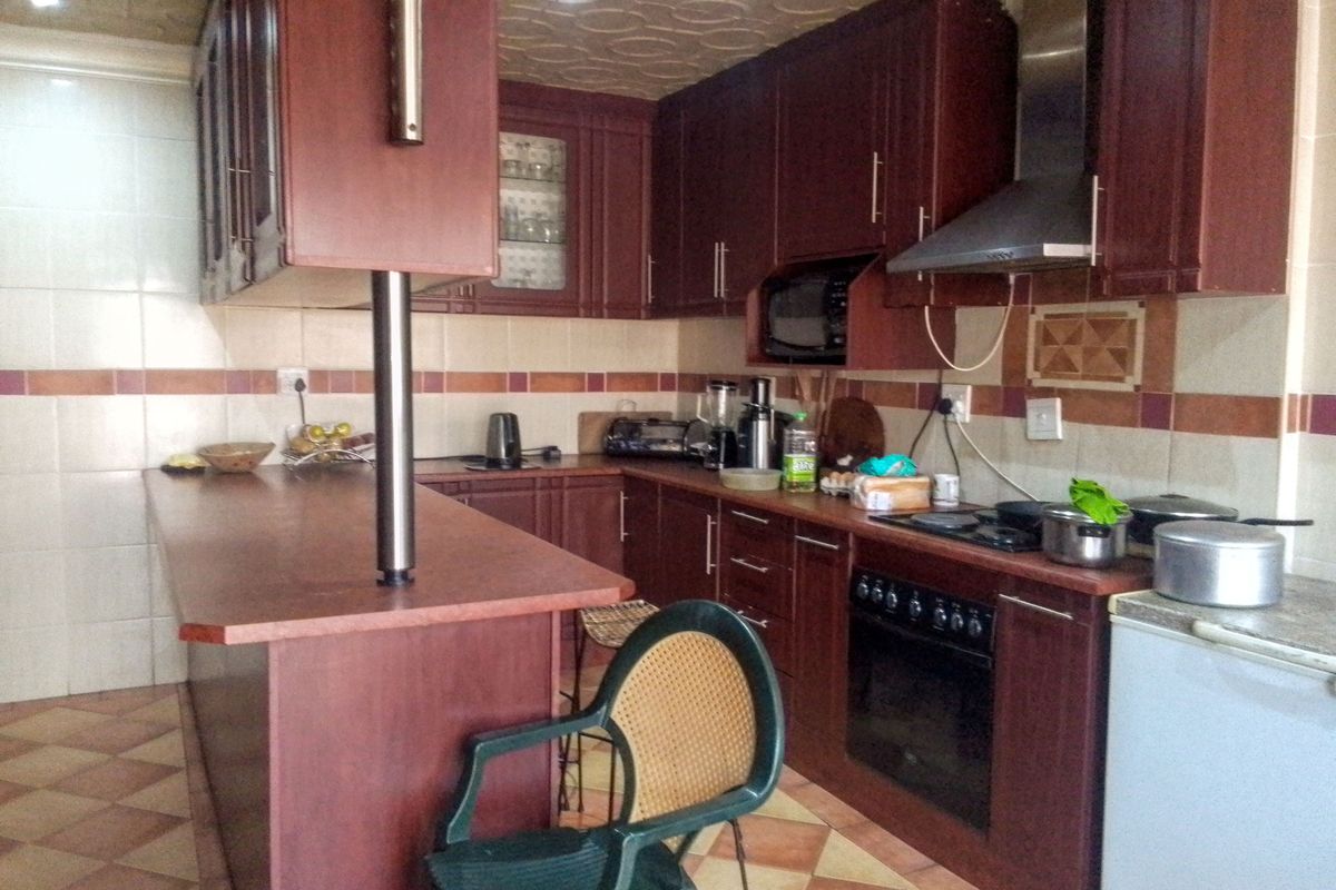 A functional kitchen featuring dark wood cabinetry, a breakfast bar, built-in oven with extractor fan, and tiled finishes throughout.
