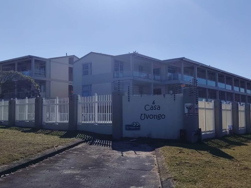 Front exterior view of the Casa Uvongo townhouse complex, featuring secure perimeter fencing, electric security wires, and multi-level residential units with balconies.