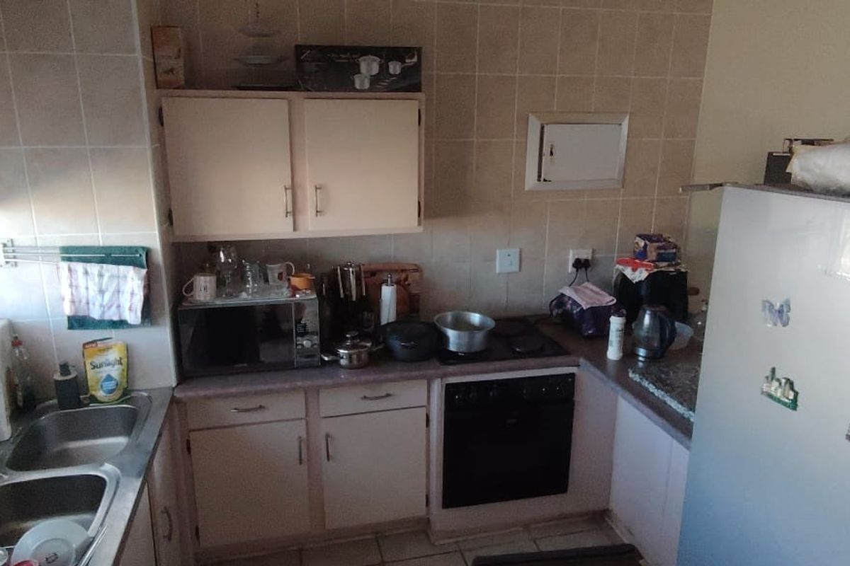 A compact kitchen featuring built-in cabinetry, a double basin sink, an electric oven and hob, and tiled splashbacks.