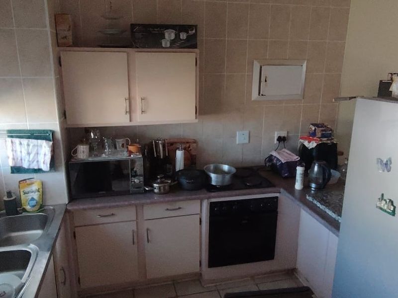A compact kitchen featuring built-in cabinetry, a double basin sink, an electric oven and hob, and tiled splashbacks.