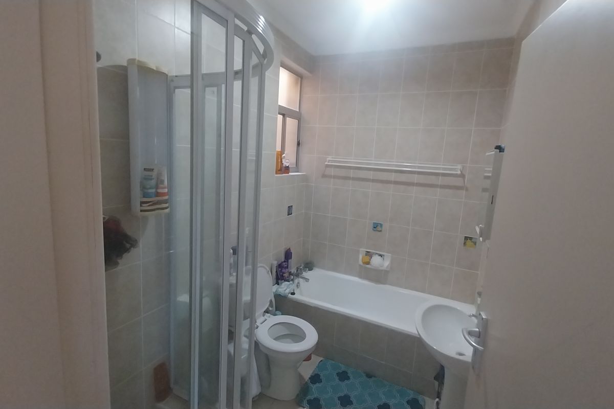 A functional bathroom featuring a shower enclosure, bathtub, pedestal basin, and toilet with neutral wall tiling.