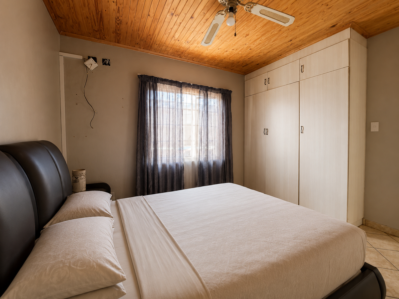 A bedroom featuring built-in cupboards, a timber ceiling with a fan, and tiled flooring. The room requires minor electrical repairs.