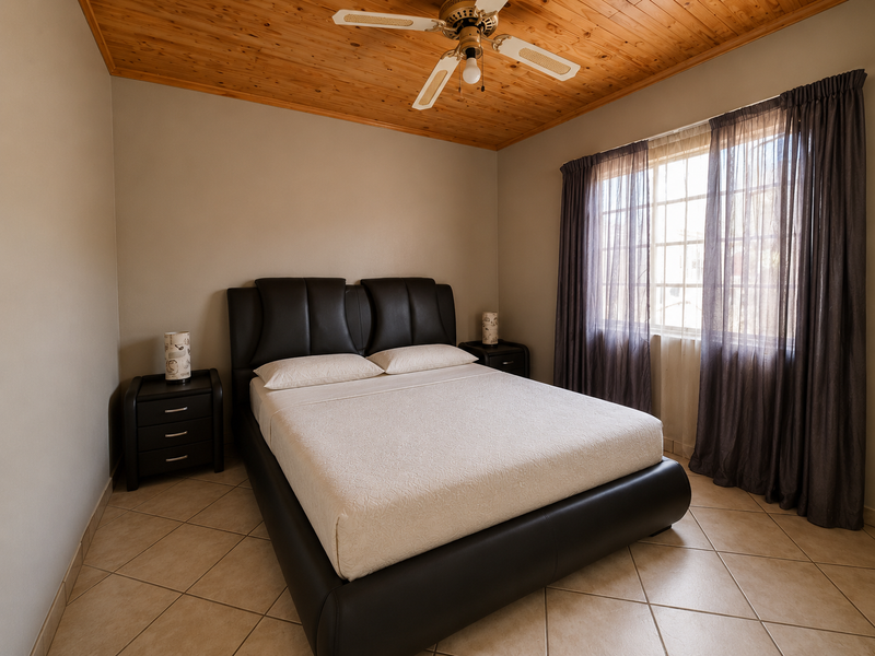 A well-maintained bedroom featuring a warm timber ceiling, ceiling fan, and neutral tiled flooring, providing a comfortable and functional living space.