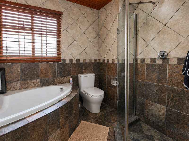 A functional bathroom featuring a corner bathtub, glass-enclosed shower, and tiled finishes throughout, offering a classic layout with natural light from the window.