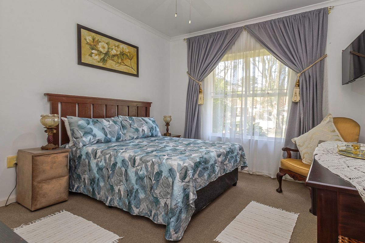 A well-lit bedroom featuring neutral wall finishes, carpeted flooring, and a large window with curtains, providing a comfortable and functional living space.