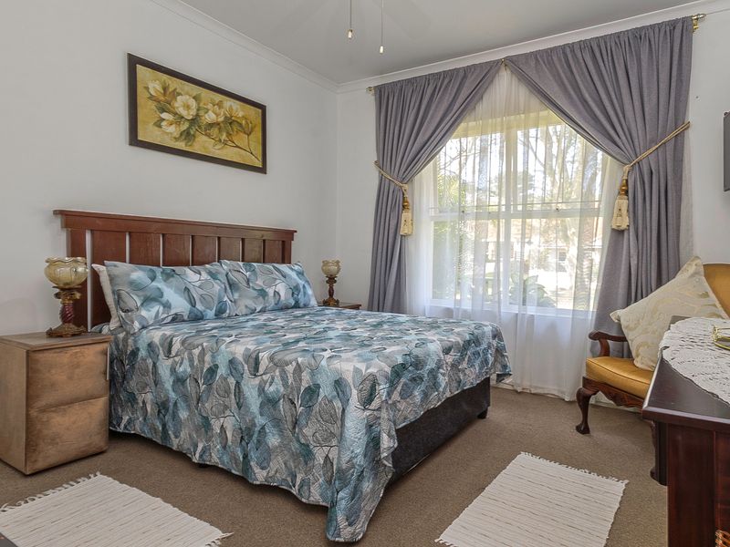 A well-lit bedroom featuring neutral wall finishes, carpeted flooring, and a large window with curtains, providing a comfortable and functional living space.
