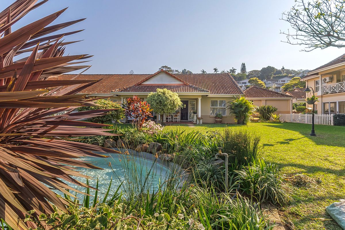 A well-maintained rear garden featuring a landscaped lawn, a water feature, and a covered patio area attached to the main residence.