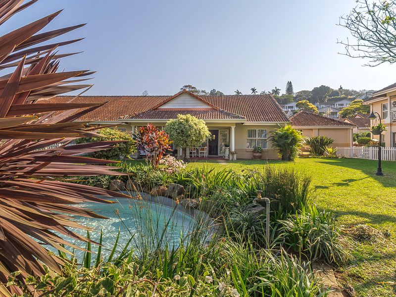 A well-maintained rear garden featuring a landscaped lawn, a water feature, and a covered patio area attached to the main residence.