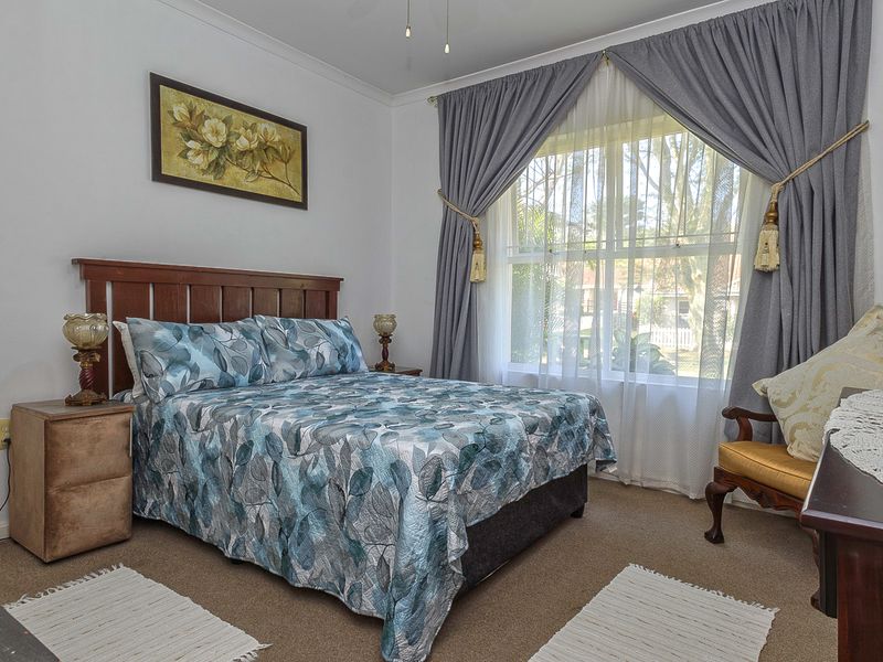 A well-lit bedroom featuring neutral carpeting, cove cornicing, and a large window with curtains, providing a comfortable and functional living space.