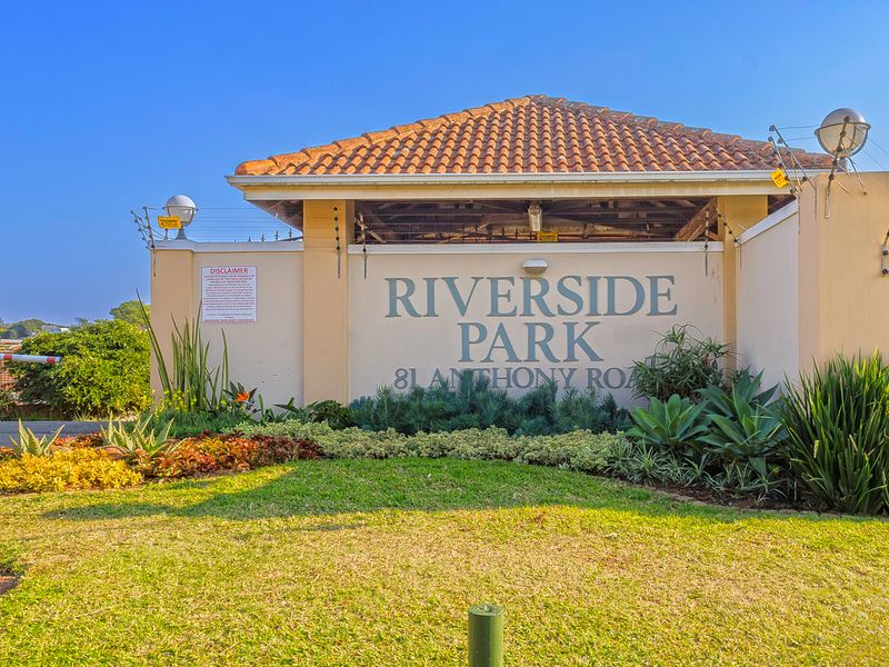 The main entrance gate and signage for Riverside Park retirement village, featuring well-maintained landscaping and security infrastructure.