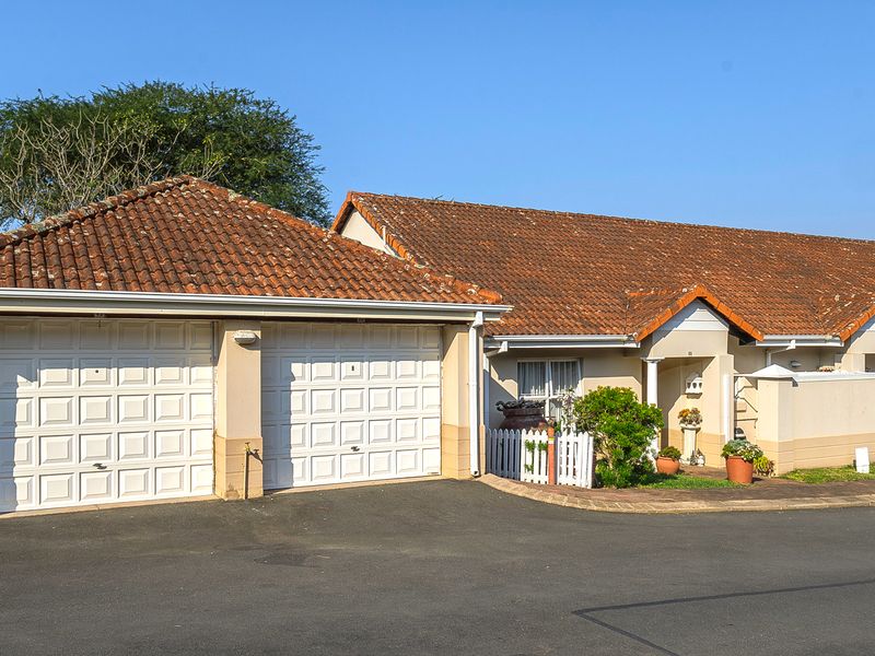 Front elevation of a retirement village unit featuring a double garage, paved driveway, and a covered entrance with a small private garden area.