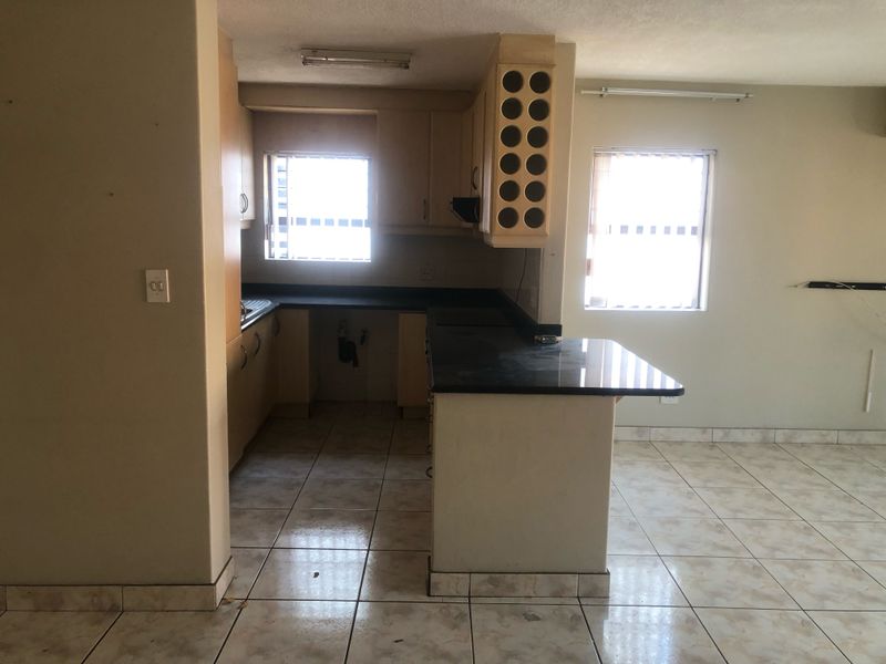 An empty kitchen featuring built-in cabinetry, a wine rack, and dark countertops, with ceramic floor tiles throughout the space.