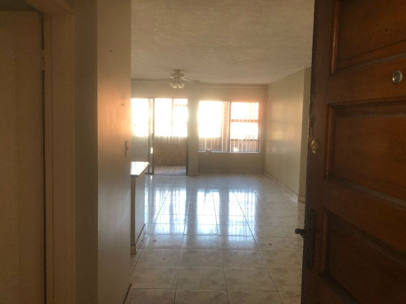 An open-plan living area featuring tiled flooring, a ceiling fan, and a sliding glass door leading to an outdoor space, viewed from the entrance.
