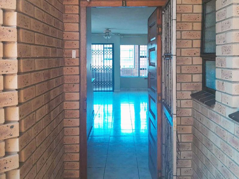 Entrance view into an open plan living area featuring face brick exterior walls, tiled flooring, and a security gate.