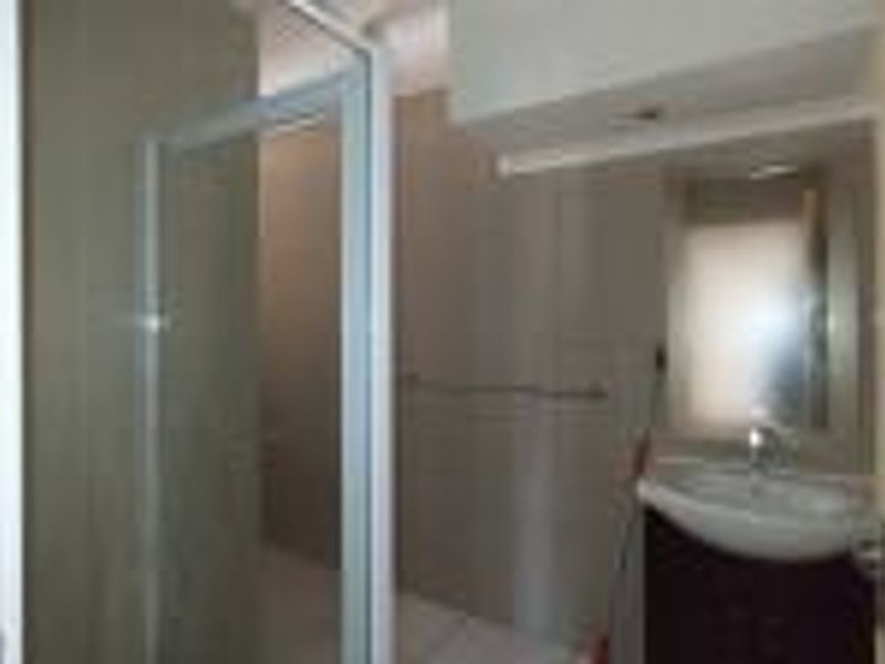 A functional bathroom featuring a shower enclosure, a vanity basin with a mirror, and neutral wall tiling.