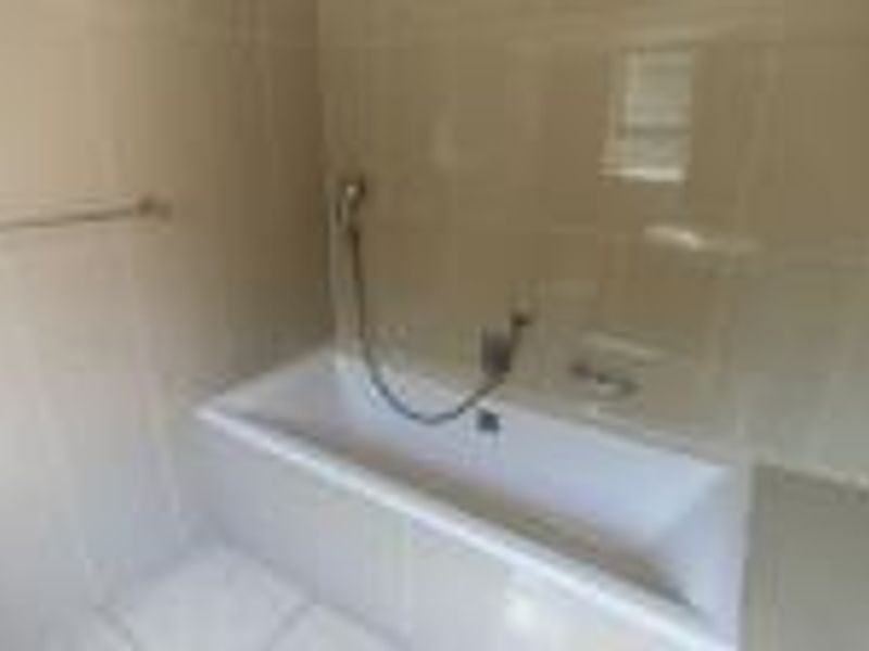 A functional bathroom featuring a built-in bathtub with shower mixer, complemented by neutral wall and floor tiling.