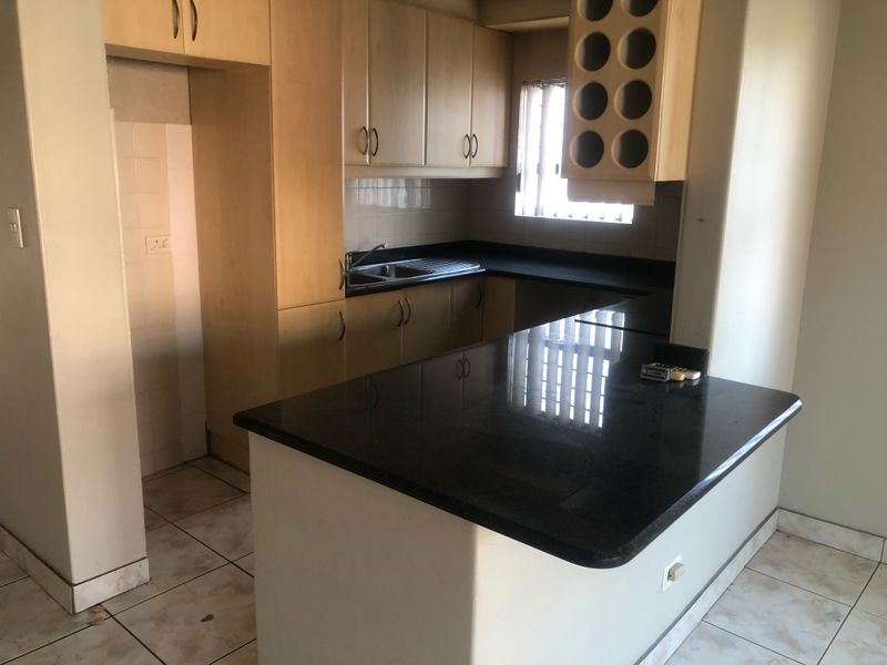 A functional kitchen featuring laminate cabinetry, granite countertops, a breakfast bar, and tiled flooring, offering a clean space ready for updates.