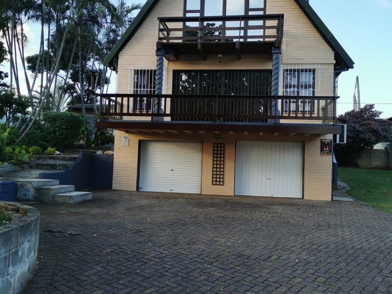 A two-story residential property featuring a double garage, paved driveway, and a prominent upper-level balcony with timber decking.