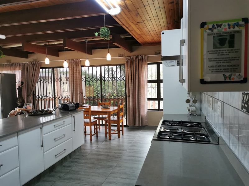 Open-plan kitchen and dining area featuring modern white cabinetry, stone countertops, gas hob, and exposed timber ceiling beams with direct access to the patio.