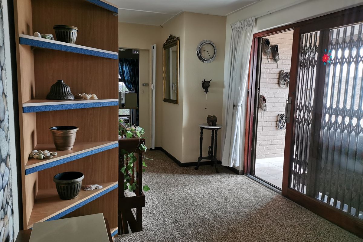 A living area featuring carpeted flooring, a sliding glass door with a security gate, and access to an adjacent staircase.