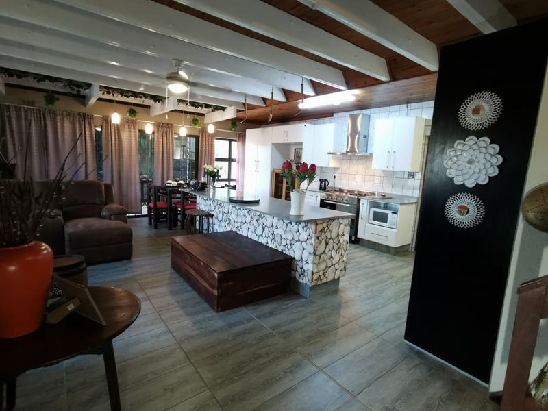 Spacious open-plan living and kitchen area featuring exposed timber ceiling beams, a modern kitchen island, and contemporary tiled flooring throughout.
