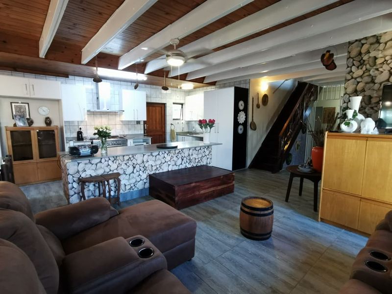 Spacious open-plan living area featuring a stone-clad kitchen island, exposed timber beam ceilings, and a striking stone feature wall with an integrated staircase.