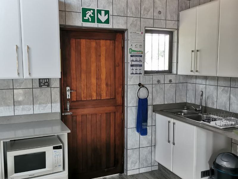 Functional scullery area featuring built-in white cabinetry, stainless steel sink, tiled splashbacks, and a timber-clad ceiling.
