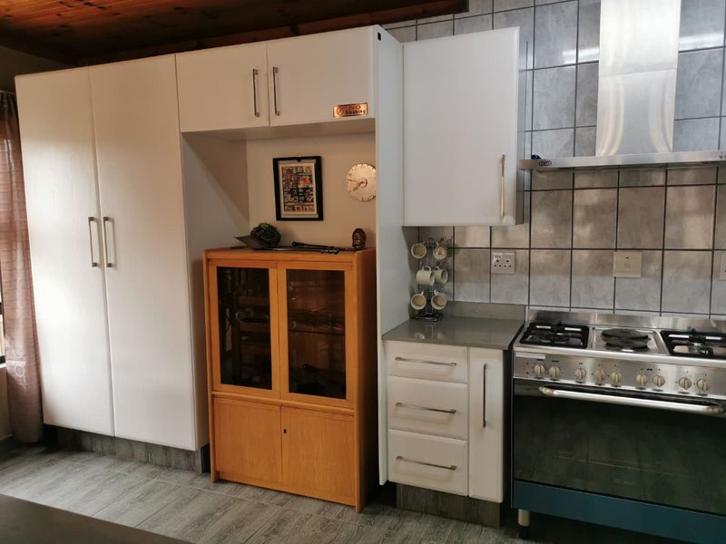 A functional kitchen featuring white cabinetry, a stainless steel extractor fan, a gas stove, and tiled backsplash with wood-look laminate flooring.