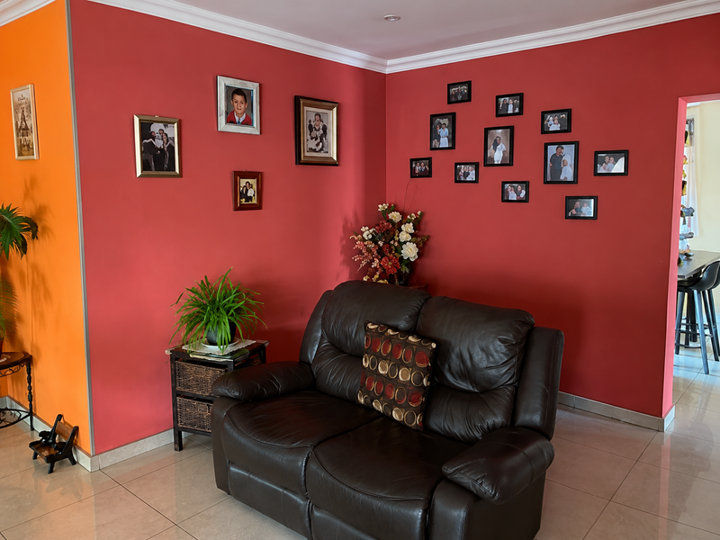 A living room area featuring tiled flooring and decorative wall finishes, providing a functional space with access to an adjacent dining area.